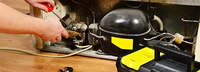 Refrigerator repair technician fixing the compressor and wiring in Fullerton, CA