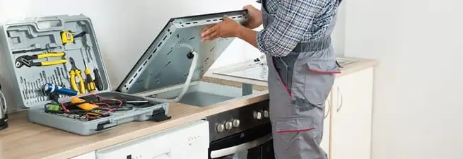 Cooktop repair technician lifting a built-in stovetop for service in Anaheim, CA