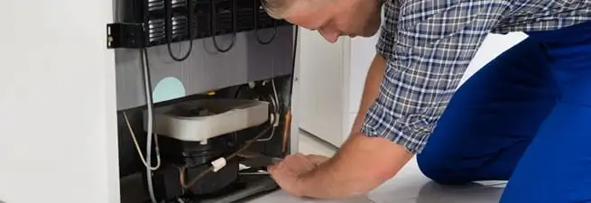 Refrigerator repair technician servicing the compressor and condenser area in Anaheim, CA