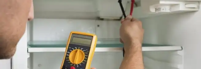 Refrigerator repair technician testing electrical components with a multimeter in Anaheim, CA