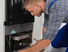 Refrigerator repair technician servicing the compressor and condenser area in Anaheim, CA